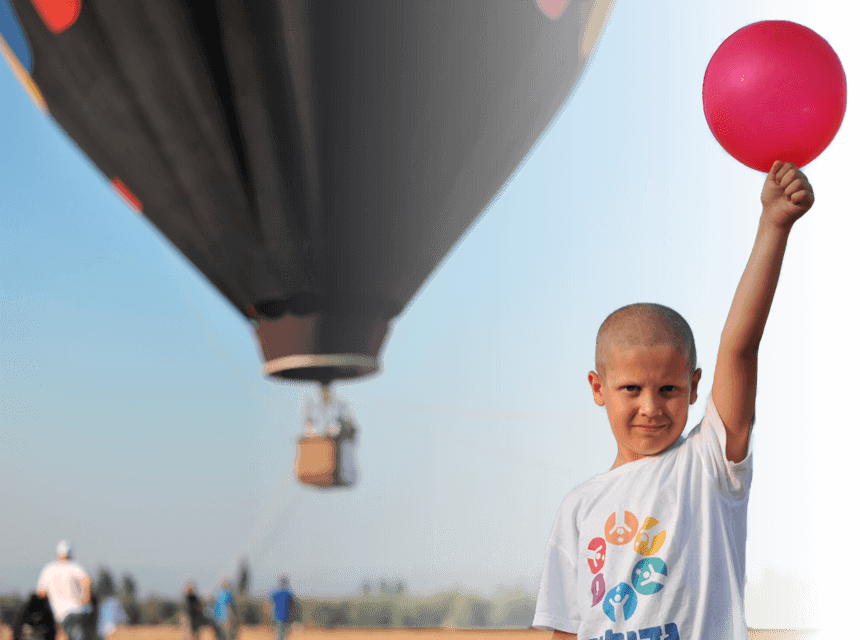 A boy in a shirt of larger-than-life holds a deep pink balloon and a hot air balloon behind him